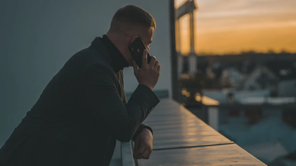 a man on the phone, leaning against a railing overlooking the water.